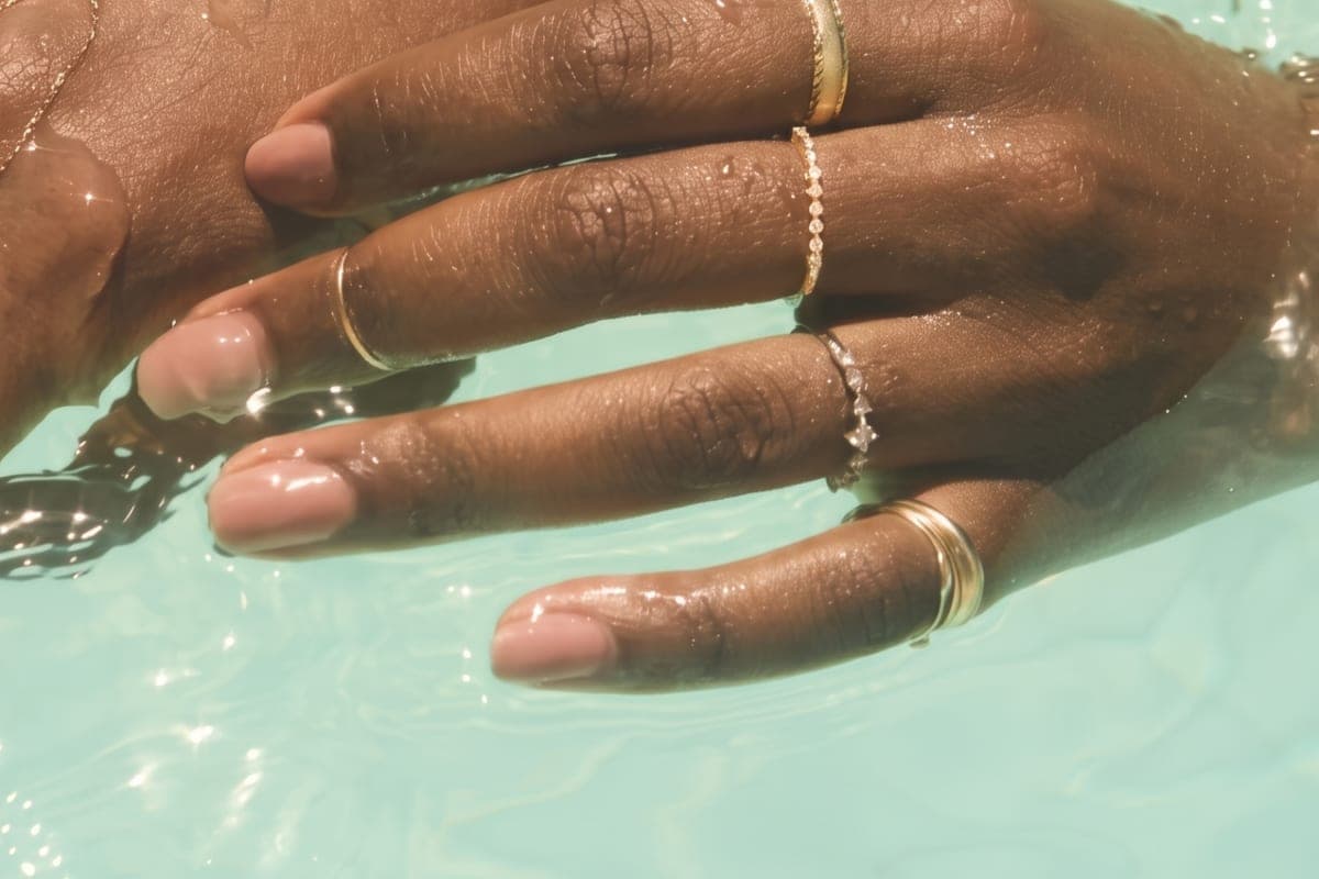 Stacked gold rings and a body chain worn in sunlit water, from the Catbird collection